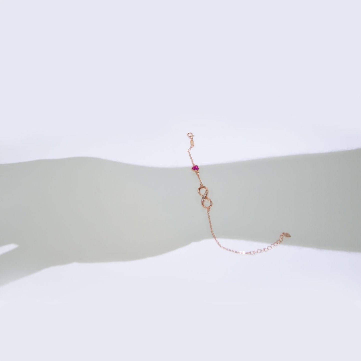Detailaufnahme eines Armbands mit Unendlichkeitszeichen in Roségold und einem roten herzförmigen Kristall, ideal für besondere Anlässe."